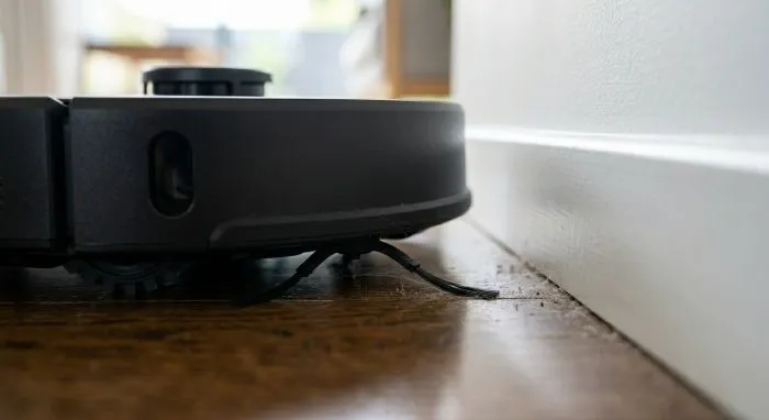  Detalle de un robot aspirador de 2026 utilizando una mopa extensible para limpiar el borde de un zócalo y una esquina de difícil acceso en una cocina de diseño.